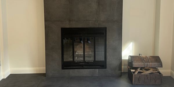 Modern fireplace with dark tiles and wooden chest filled with firewood.