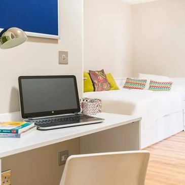 Minimalistic workspace with laptop, books, and a cozy bed in a bright room.