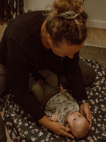 Adult comforting a baby lying on a patterned cushion.
