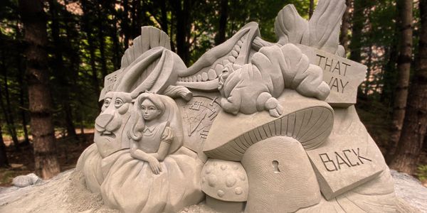 An alice in wonderland sand sculpture with a fall forest in New Hamsphire in the background