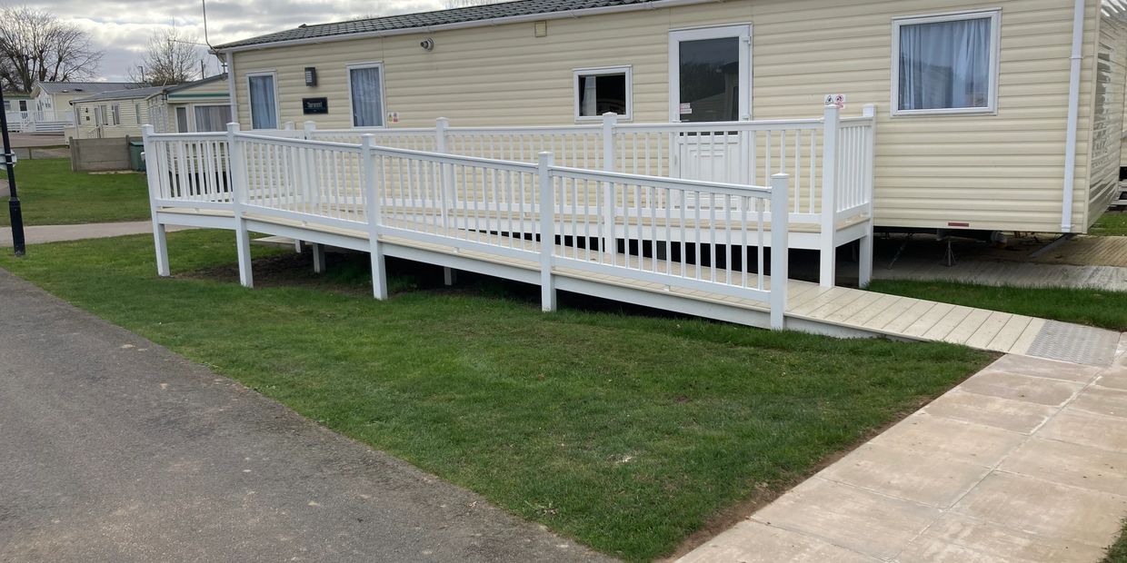 A beige mobile home with a white wheelchair-accessible ramp on green grass.