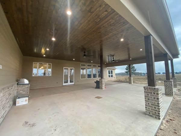 Spacious covered patio with wooden ceiling and brick pillars.