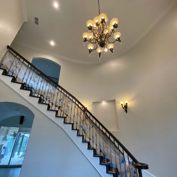 Elegant staircase with ornate railing and a classic chandelier in a spacious home.