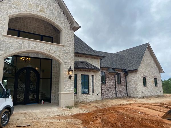 Large stone and brick house under construction with arched entrance and black iron doors.