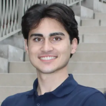Young man smiling outdoors with stairs in background.