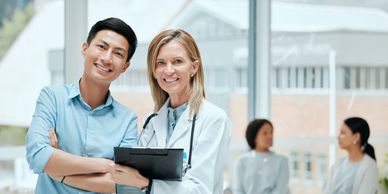 Two smiling healthcare professionals posing with clipboards in a bright medical setting.