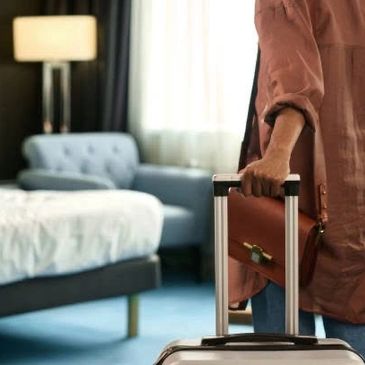 Person holding suitcase handle in a hotel room.
