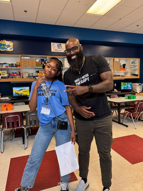 A smiling man and a girl posing with peace signs in a classroom.