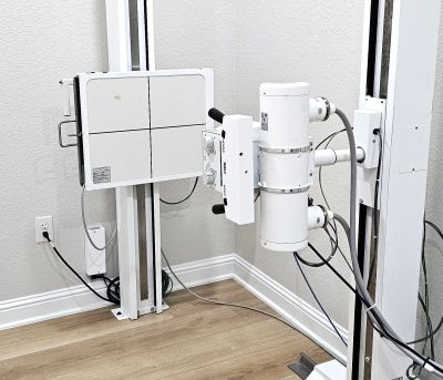 Modern X-ray machine mounted in a clinical room with wooden flooring.