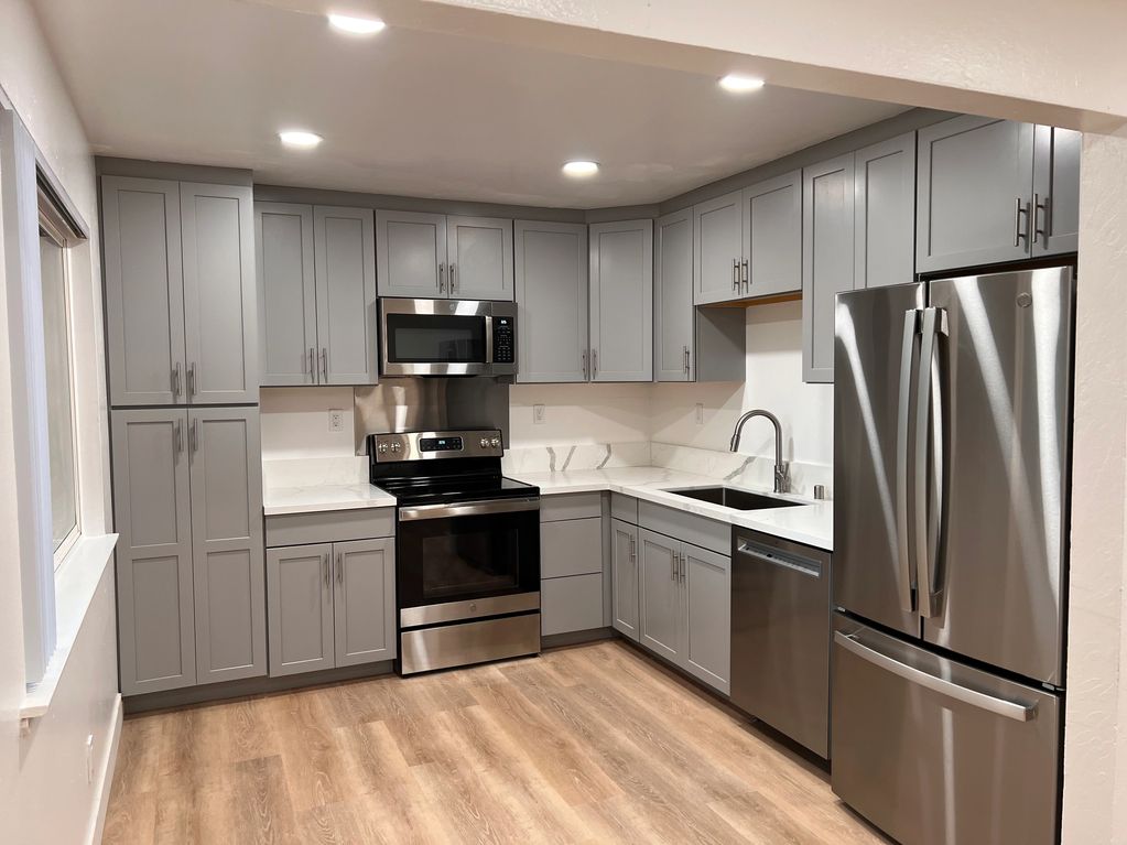 A remodeled kitchen with grey modern cabinets, brand new appliances, and marble countertops