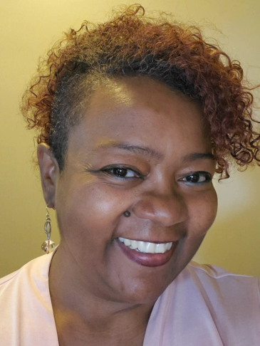 Smiling woman with curly hair and piercing.