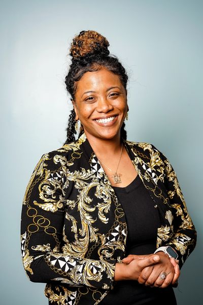Smiling woman Dr.Dicks with curly hair bun and patterned jacket.