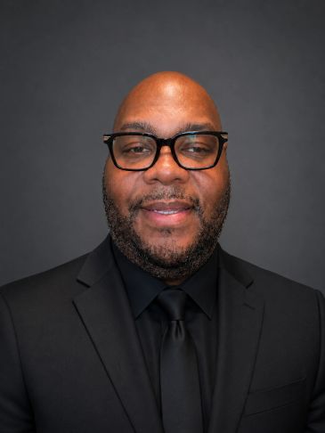 Smiling man in black suit and glasses.