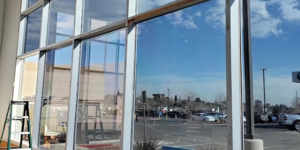 Large glass windows reflecting a parking lot and blue sky.