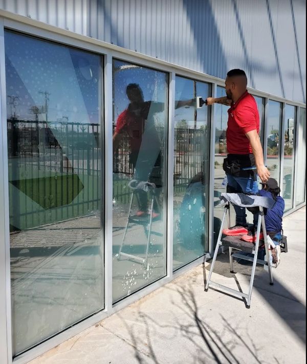 Two men cleaning large glass windows outside a building.