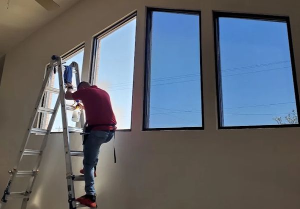 A man on a ladder cleaning tall windows indoors.