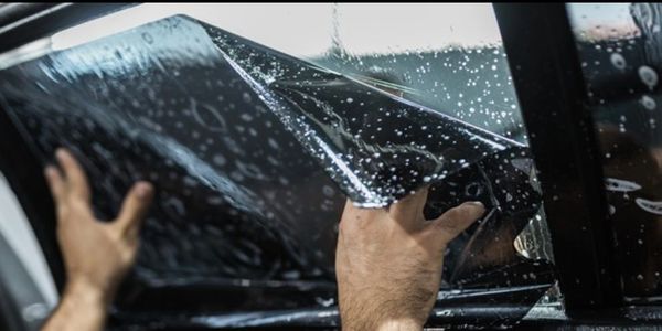 Hands applying a tinted film on a car window.