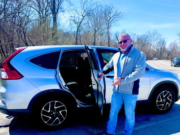 Man in sunglasses standing by an open car door outdoors.