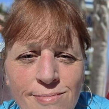 Close-up of a woman smiling outdoors in sunlight.