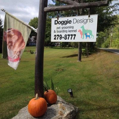Sign for Doggie Designs grooming and boarding with pumpkins and a dog flag.