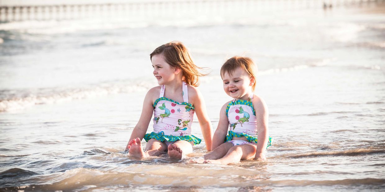 Family beach portrait of kids , sisters playing in the ocean by the seashore at Topsail Island NC