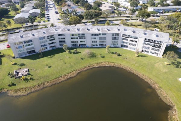 Curved residential building overlooking a calm pond with green lawn.