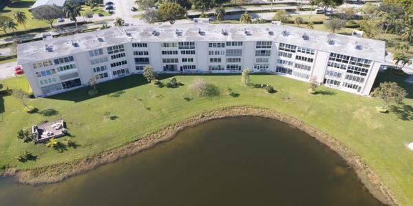 Curved residential building overlooking a calm pond with green lawn.