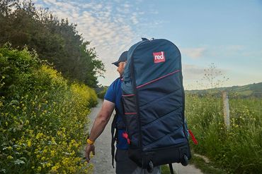 customer walking to the lake with there red paddle board supplied by explore the lakes.