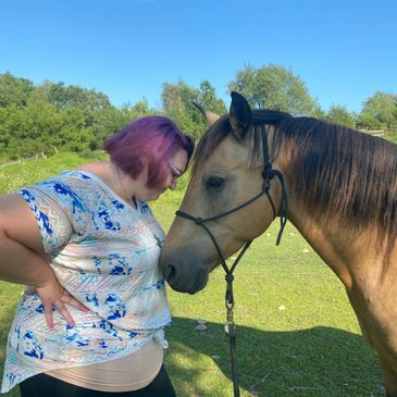 A woman and a horse stand facing each other in deep connection with eye contact. 