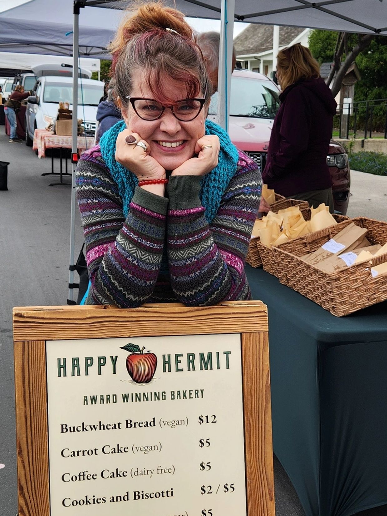 Smiling woman at a market stall with a bakery sign.