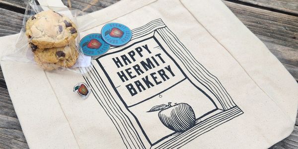 Canvas tote bag from Happy Hermit Bakery with cookies and stickers.