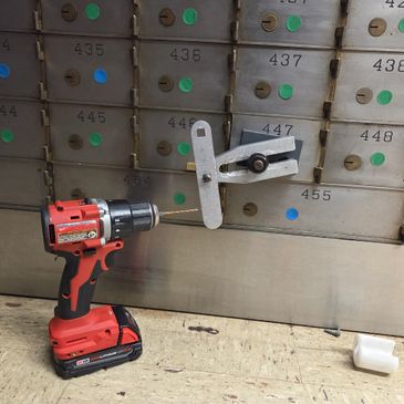 A drill with a metal attachment placed in front of a bank safety deposit box.