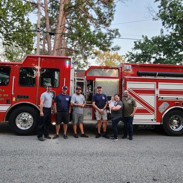 Group photo of firefighters standing in front of a red fire truck outdoors.