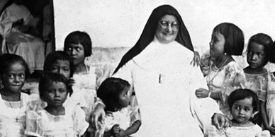 A nun surrounded by young girls in traditional dresses, smiling warmly.