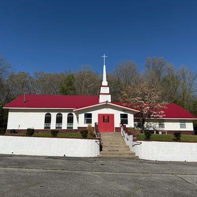A white church with a red roof and cross steeple under a clear blue sky.