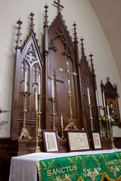 Ornate church altar with brass candlesticks, cross, and a green cloth embroidered with SANCTUS.