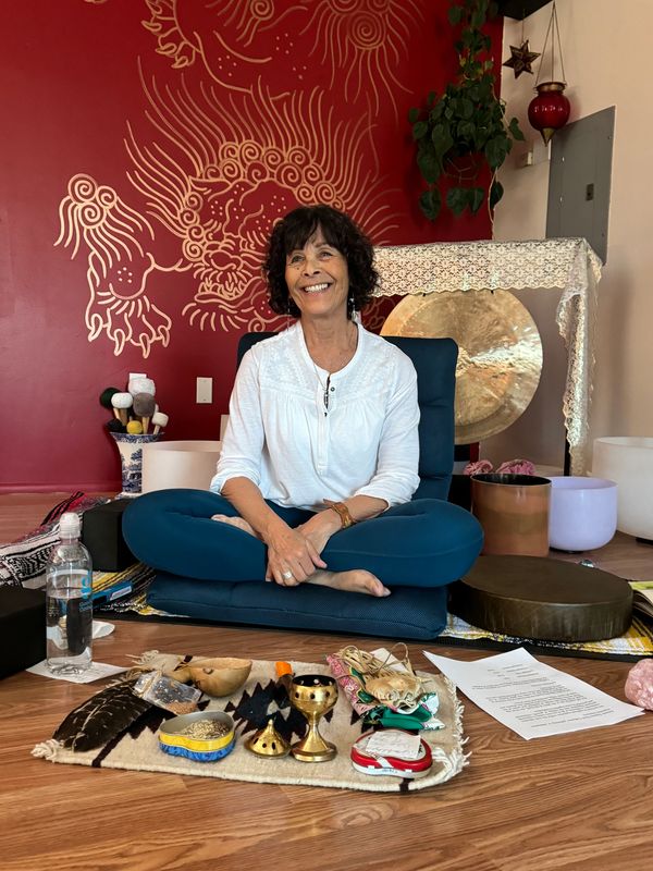 Woman sitting cross-legged on a cushion surrounded by spiritual items.