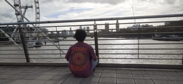 Person sitting on a bridge overlooking the Thames River with the London Eye and Big Ben in the backg