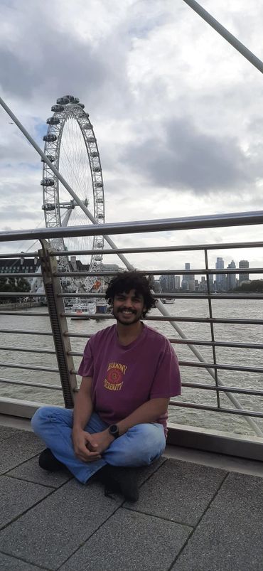 A man smiles sitting cross-legged on a bridge with the London Eye in the background. Meditation all 