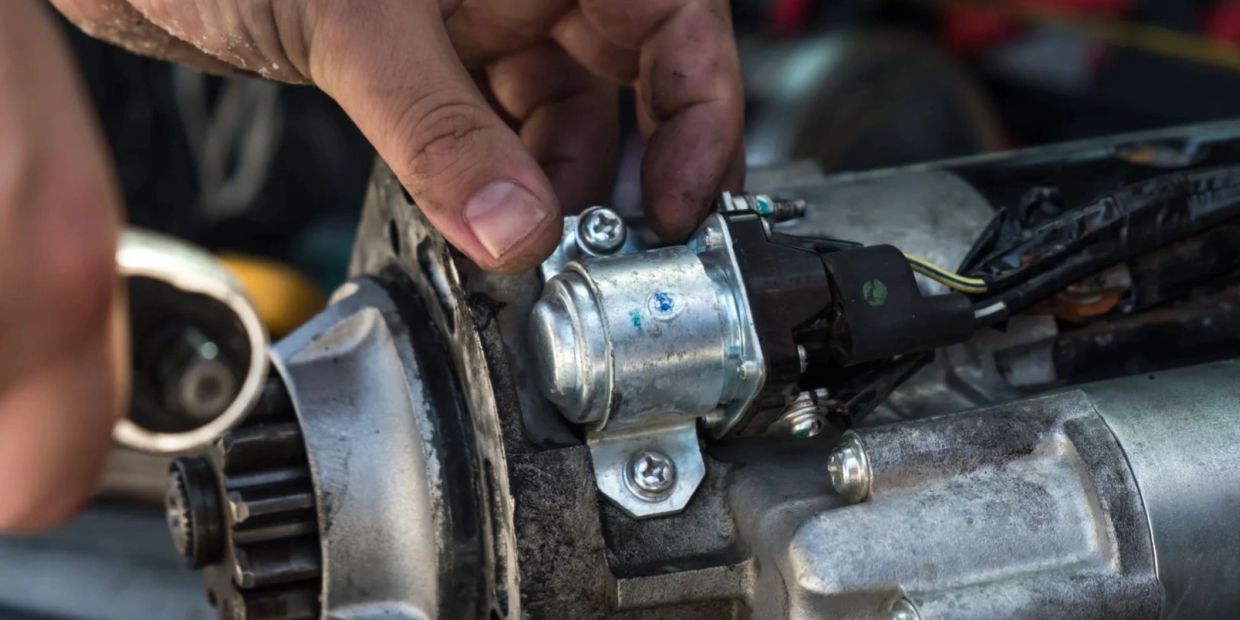 Close-up of a hand working on a metal engine part with screws and wires.
