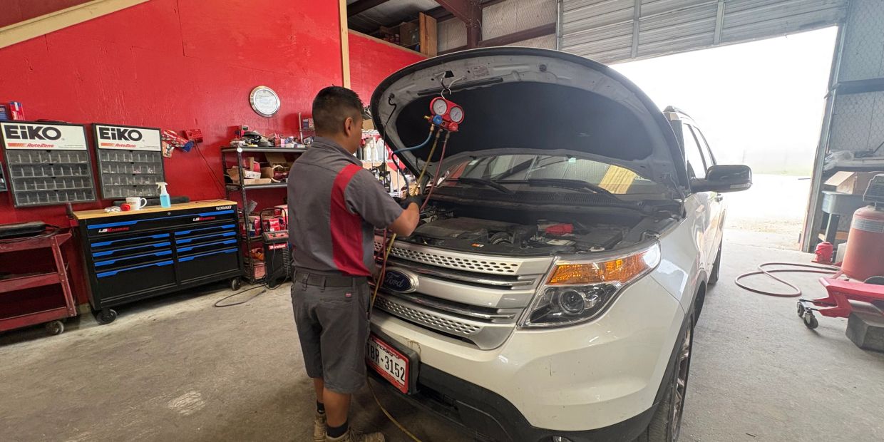 Mechanic checking a white Ford SUV's engine with diagnostic gauges in a workshop.