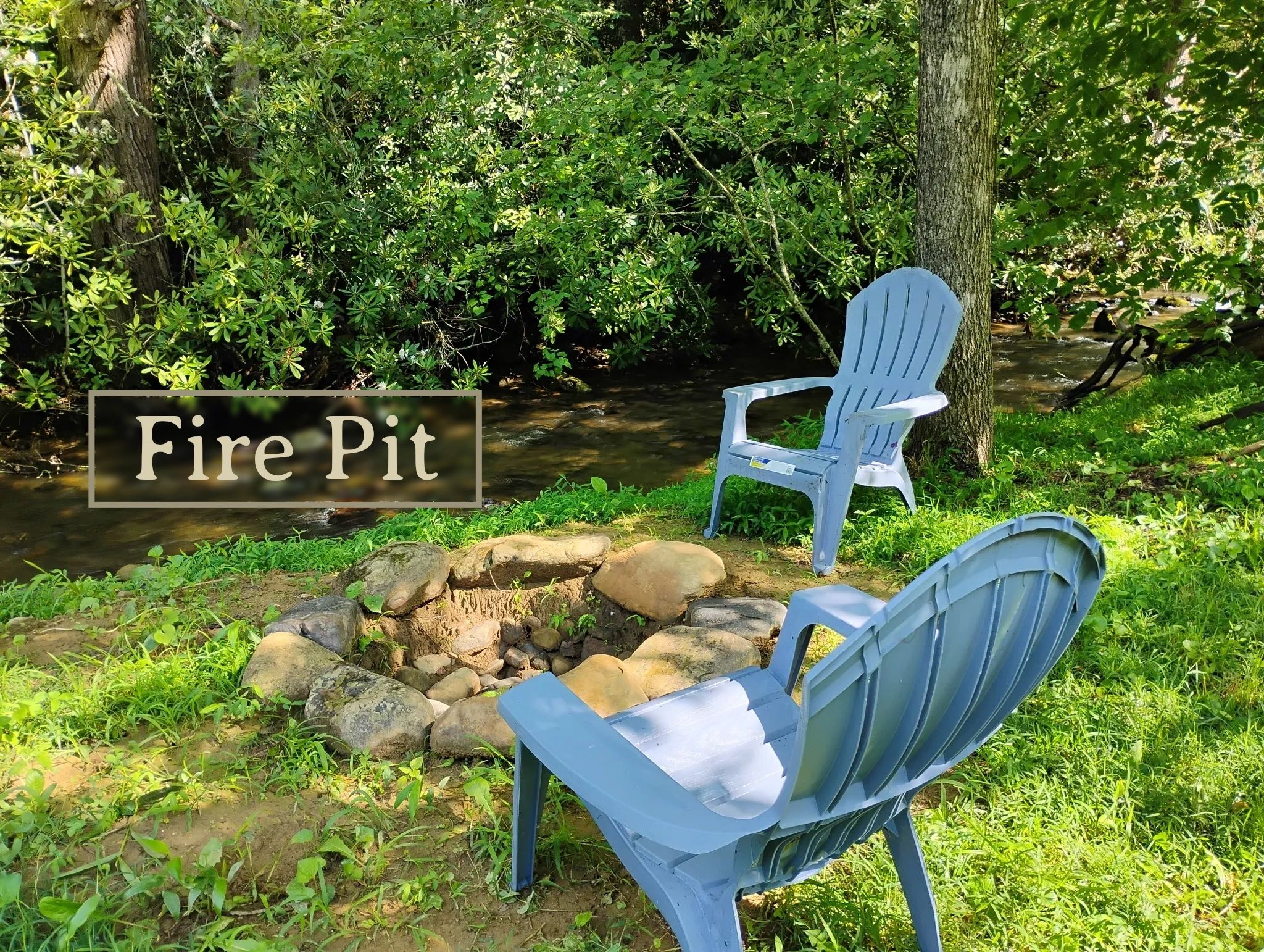 Two blue chairs around a stone fire pit by a creek in a green forest.