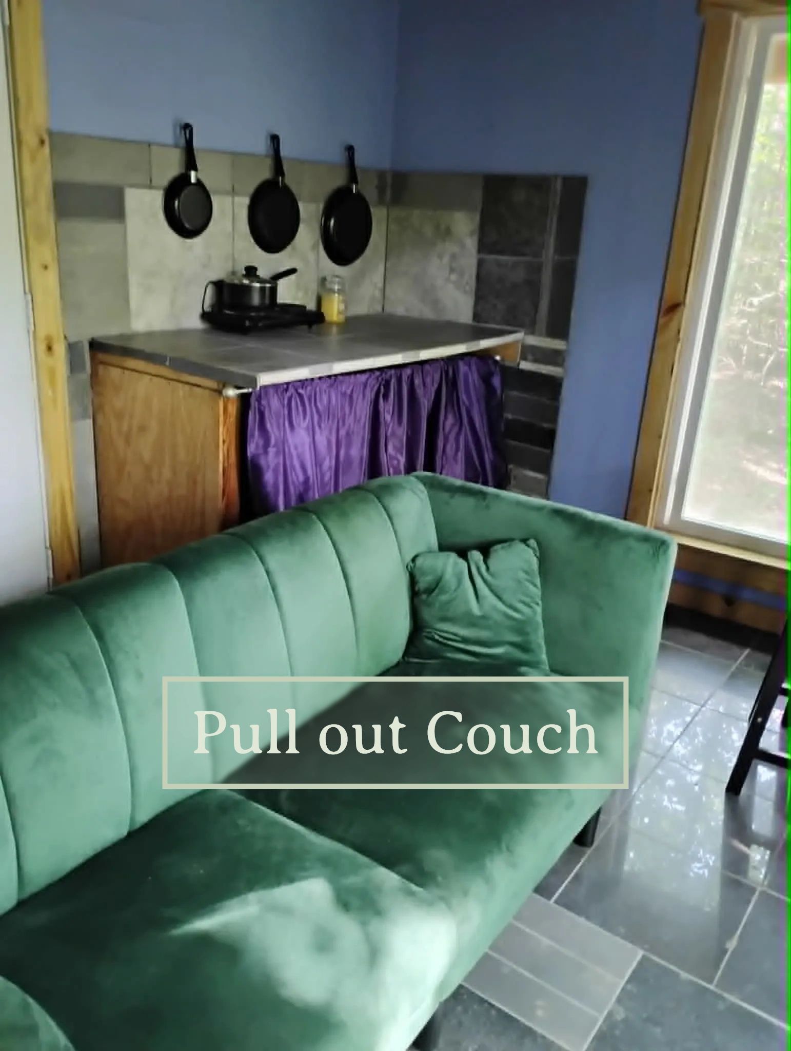 Cozy green pull-out couch in a compact kitchen corner with hanging pans.