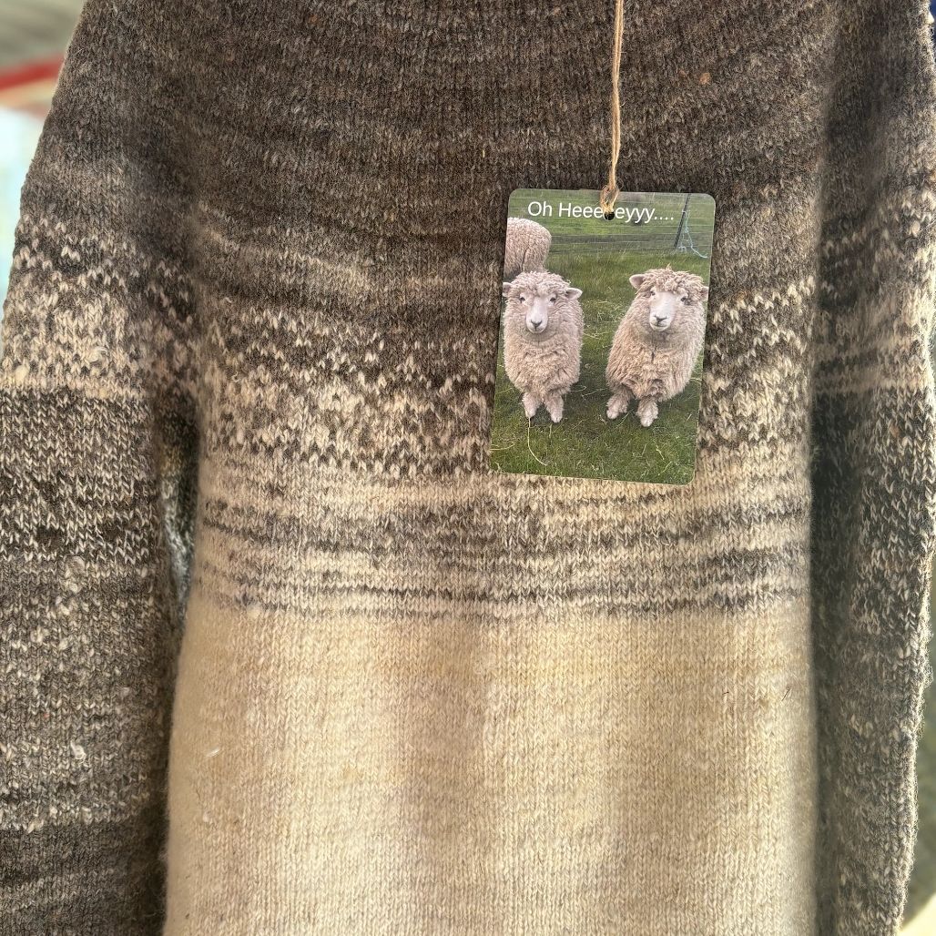 Brown and beige knitted sweater with sheep-themed tag.