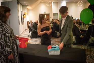 Young man and woman at a formal event, unwrapping a gift basket.
