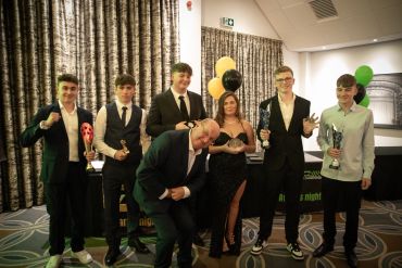 Group of young adults dressed formally holding trophies at an awards event.