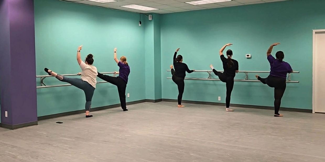 Group of women practicing ballet at barre.