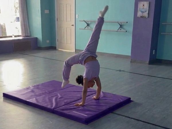 Child practicing a handstand on a purple mat indoors.