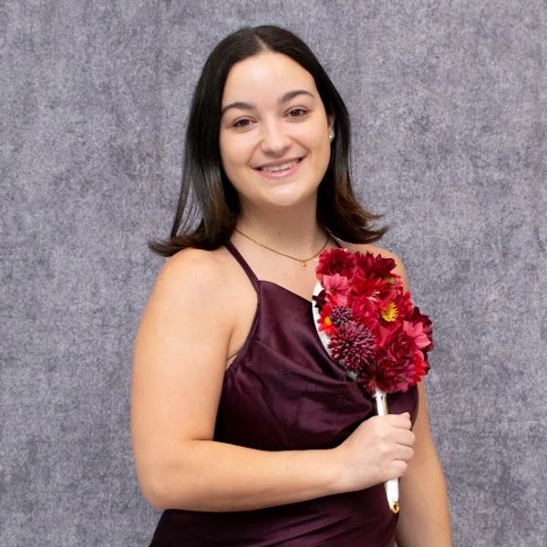 Young woman in maroon dress holding red flower bouquet.