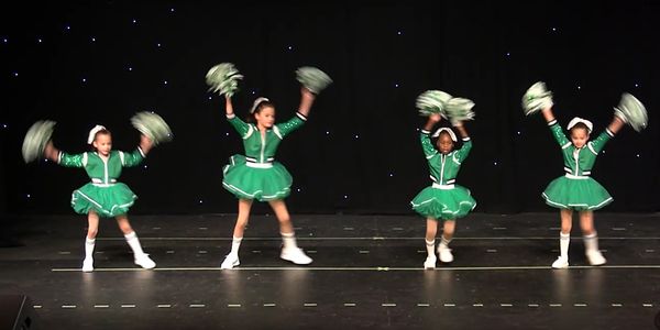 Four young cheerleaders in green performing on stage.